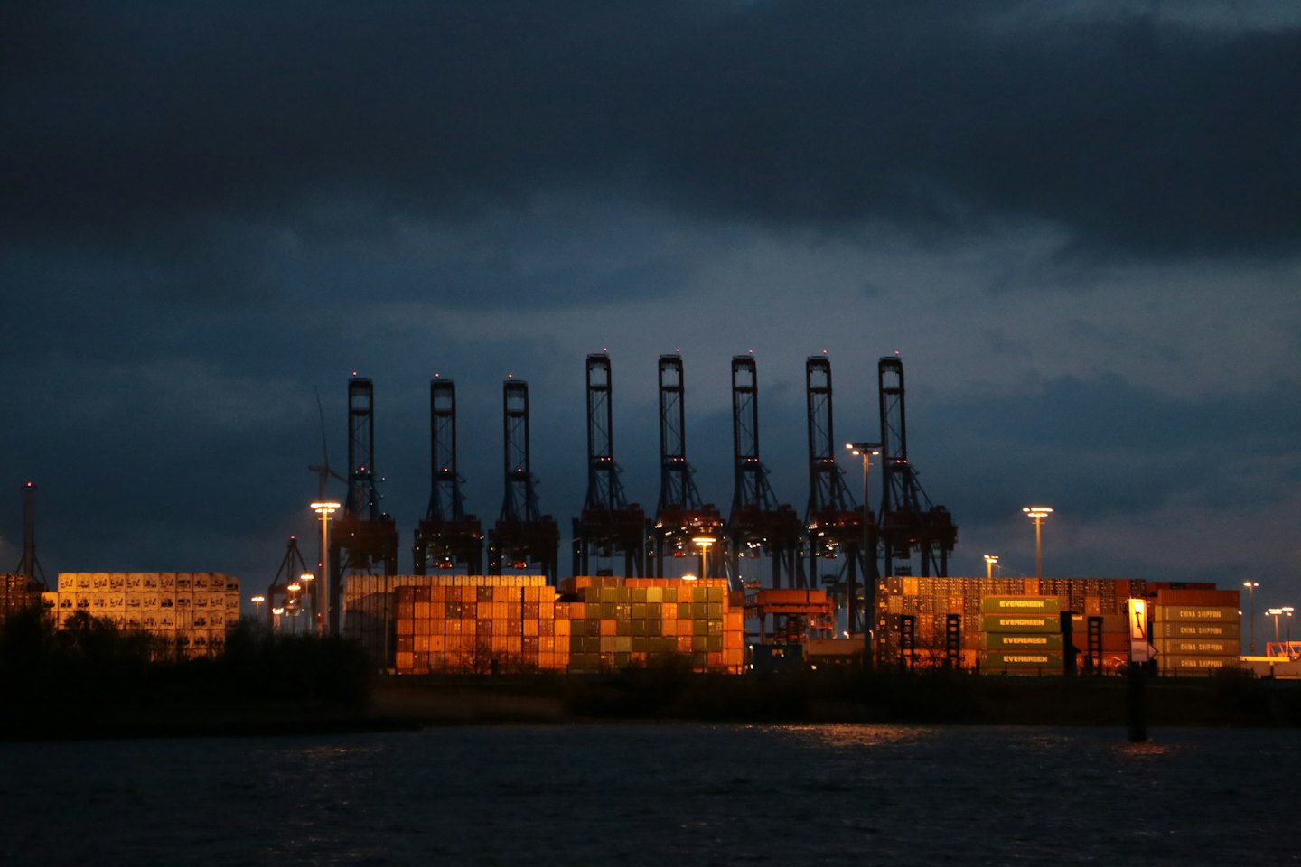 Gantry cranes stand over shipping containers at a busy port.