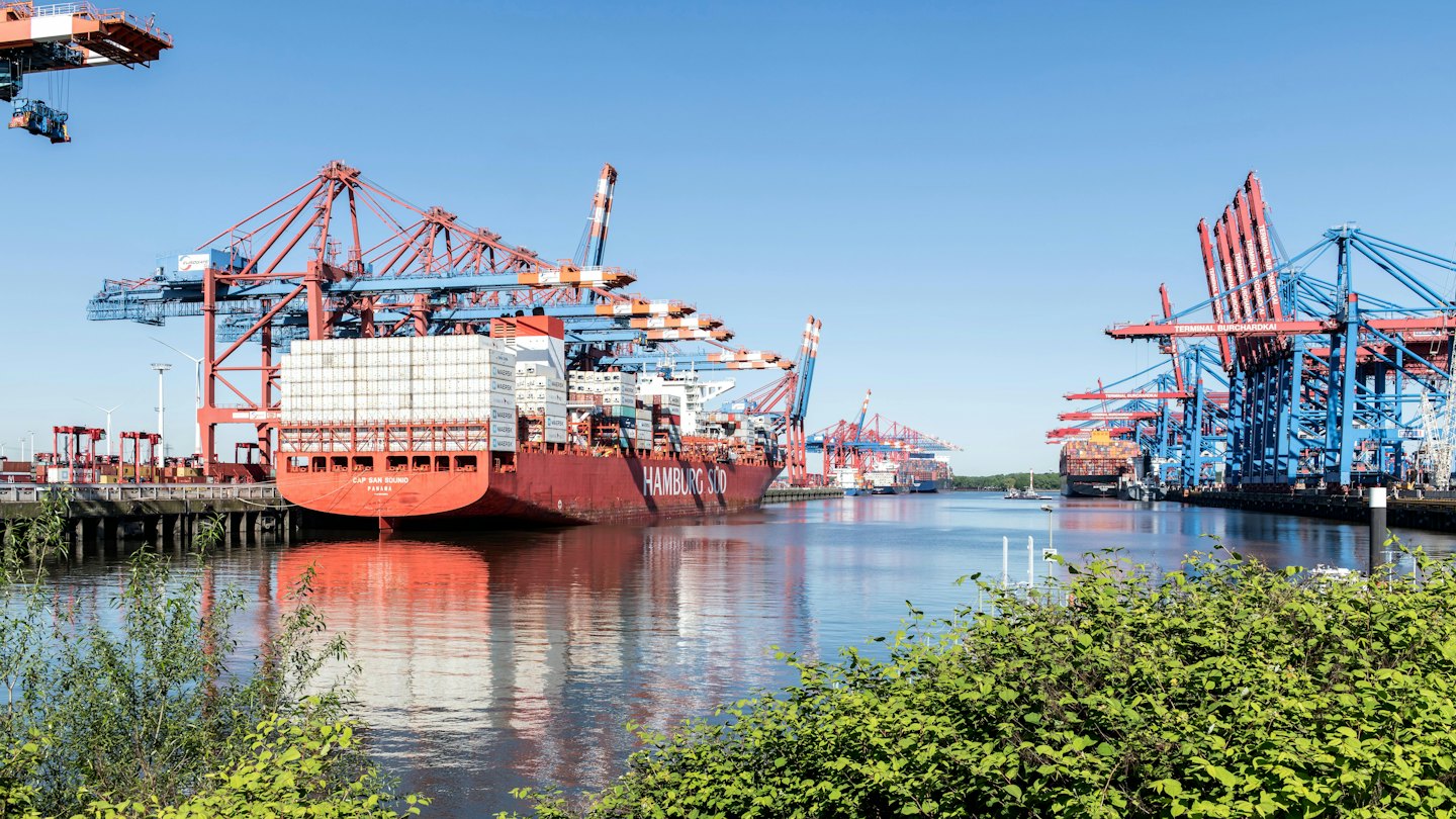 Container ship being loaded at a busy port under a blue sky.